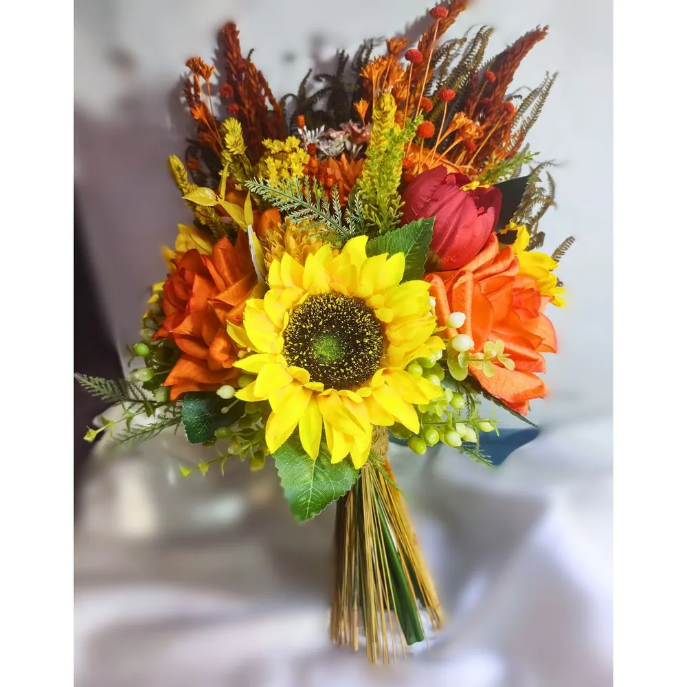Buquê redondo semirrealista com girassol no centro, rosas laranja, tulipa vermelha e frutinhas verdes