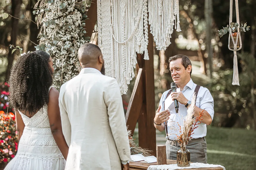 Casal em cerimônia de casamento ao ar livre enquanto o celebrante fala