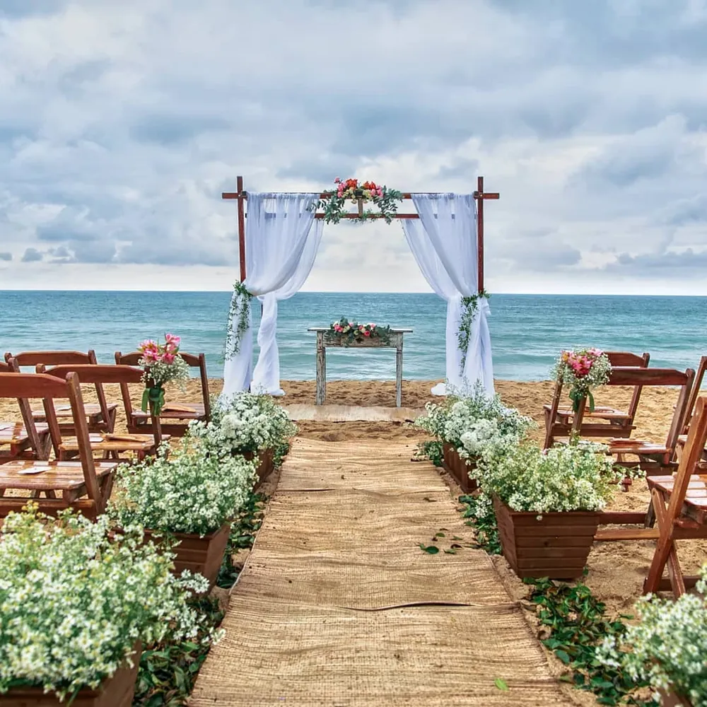 Cerimônia de casamento na praia com decoração simples e convidados sentados em bancos de madeira