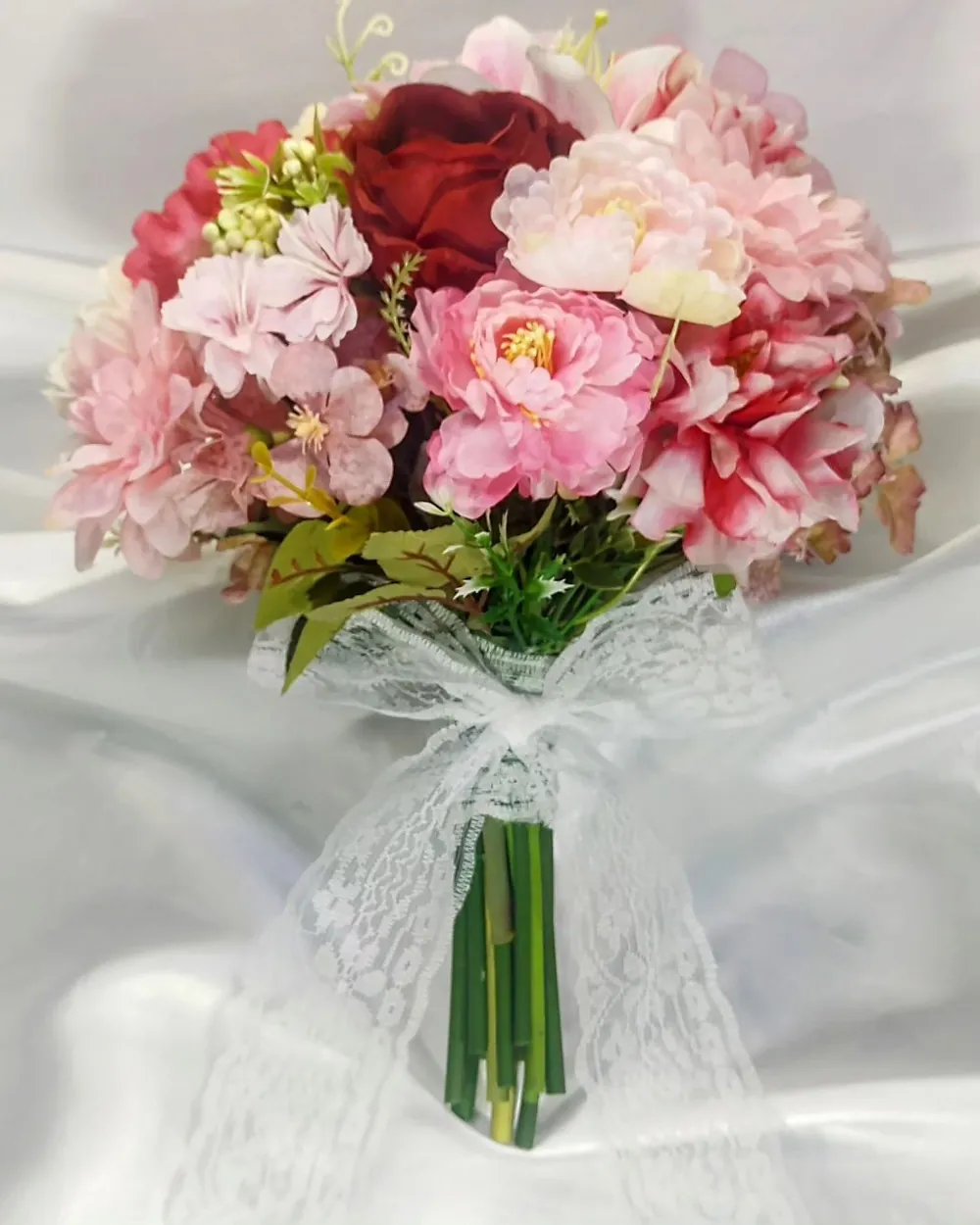 Buquê de noiva semirrealista com rosas vermelhas, rosas e cor-de-rosa, finalizado com renda branca
