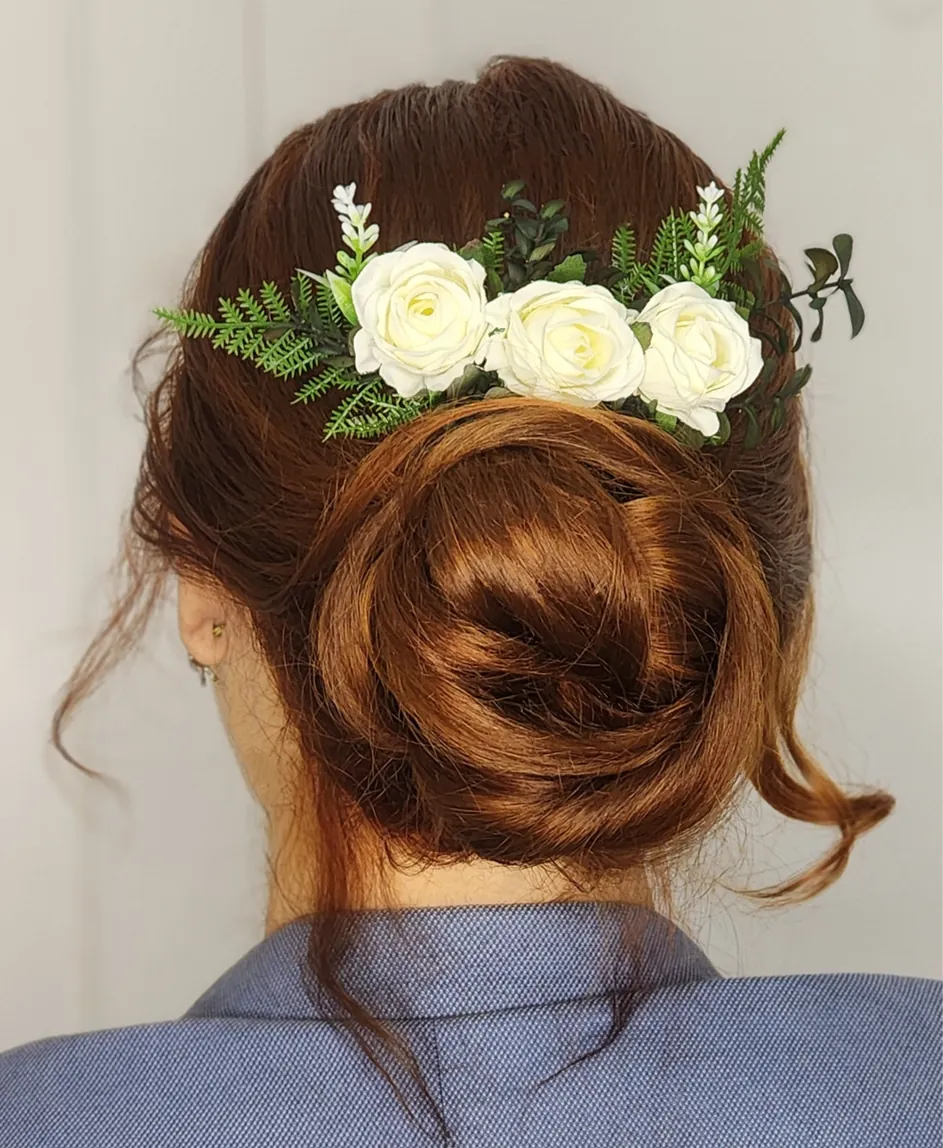 Grinalda de rosas brancas com folhagens verdes presa em um coque baixo de cabelo ruivo