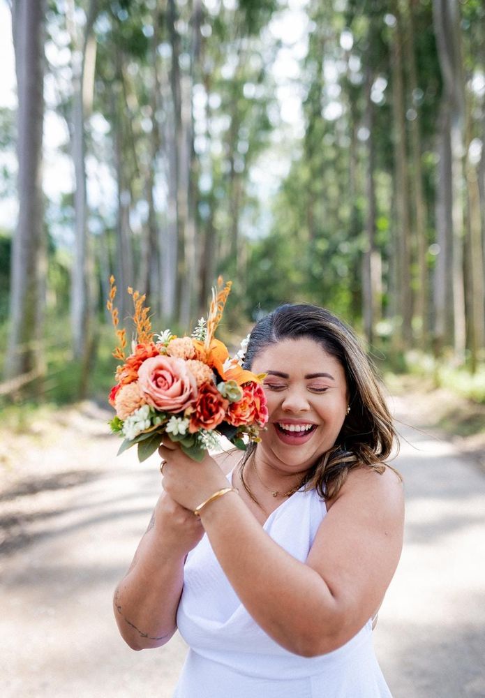 Noiva sorrindo com buquê desconstruído em tons de laranja num casamento ao ar livre